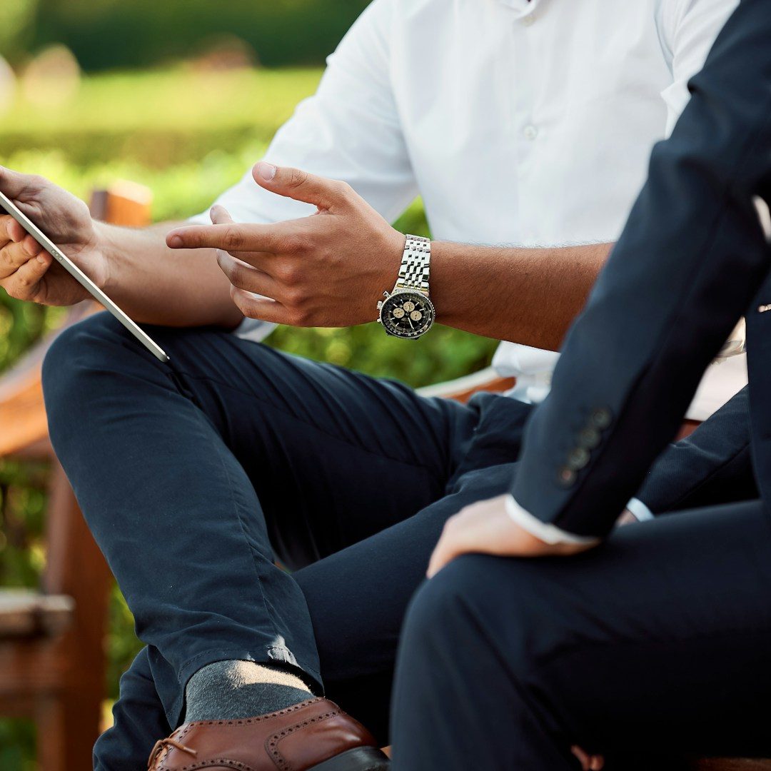 Two men having a consultation Two men in casual and formal attire discussing a tablet outdoors, surrounded by greenery.