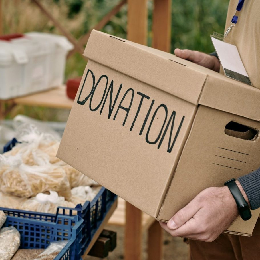 Charity IT Support Cardboard box labelled 'DONATION' held by a person, surrounded by food items.