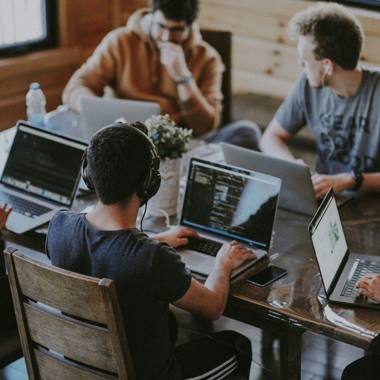 An IT Team Working A group of people collaborating at a table with laptops and a plant centerpiece.
